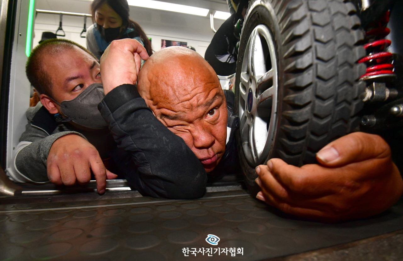 〈우수상 - "저희도 함께 살아가고 싶습니다"〉 서울 지하철 2호선 시청역에서 출근길 지하철 탑승 시위를 재개한 전국장애인차별철폐연대(전장연) 회원들이 휠체어에서 내려 지하철에 기어서 탑승한 뒤 휠체어의 바퀴를 잡고 있다. 당시 휠체어에는 문애린(42)씨가 타고 있었으며, 지하철 탑승 시위에 항의하는 한 시민에게 "죄송합니다, 저희도 함께 살아가고 싶습니다"라고 대답하고 있었다. 이 모습을 본 전장연 회원들은 기어서 문 씨의 휠체어 바퀴를 잡는 모습을 담아냈다. 〈최현규기자 / 국민일보 / 한국사진기자협회〉