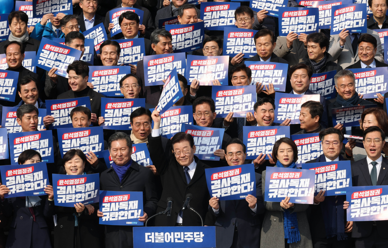 Lee Jae-myung (front row, fourth from left), chairman of the Democratic Party of Korea, raises his hand to greet at the rally to criticize Yoon Suk Yeol regime and prosecution held in front of the National Assembly's main office, Friday. Lawmakers and party officials at the rally are holding a hand sign that reads, "condemn the prosecution dictatorship." (Yonhap)
