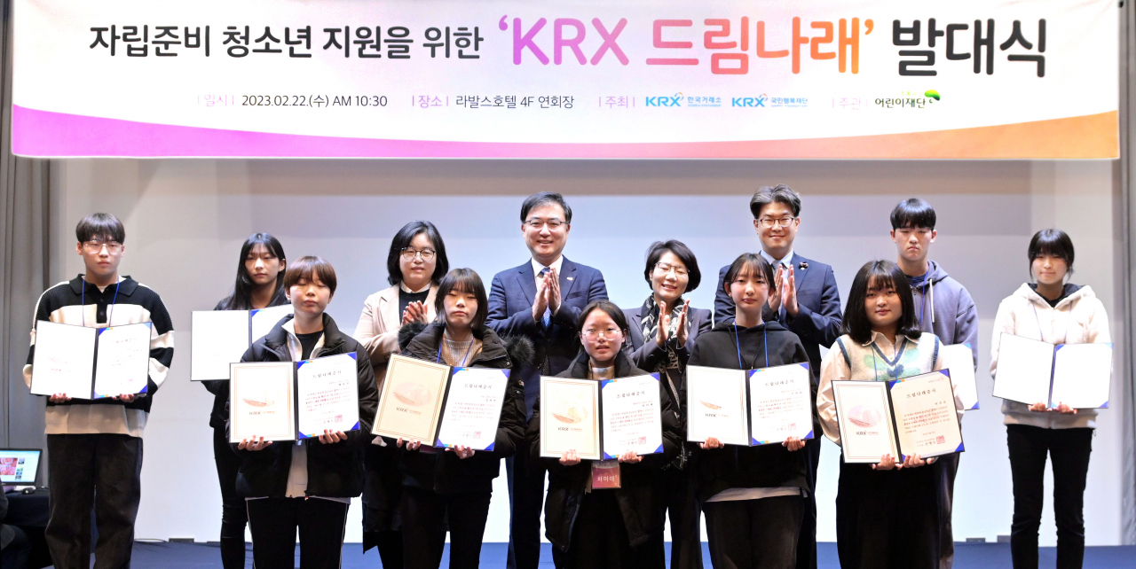 황우경(뒷줄 왼쪽에서 세번째부터 순서대로) KRX국민행복재단 사무국장, 손병두 한국거래소 이사장, 송숙희 부산시 여성특별보좌관, 노희헌 초록우산어린이재단 부산지역본부 본부장이 22일 부산 라발스호텔에서 열린 KRX 드림나래 2기 발대식에서 선정된 청소년 10명에게 증서를 전달하고 기념촬영을 하고 있다. 이날 한국거래소는 보호종료 청소년 자립 지원금 2억원을 초록우산어린이재단 부산지역본부에 전달했다. [한국거래소]