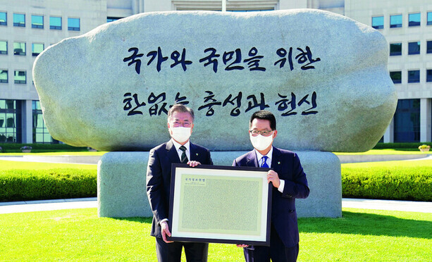 문재인 전 대통령이 지난 2021년 6월4일, 국가정보원에서 열린 국정원 원훈석 제막식에서 박지원 전 국정원장과 함께 개정된 국정원법을 새긴 동판을 들고 기념사진을 찍고 있다. 국정원 원훈은 5년 만에 ‘국가와 국민을 위한 한없는 충성과 헌신’으로 교체됐고, 원훈석의 글씨는 국가보안법 위반으로 무기징역을 선고받았던 고 신영복 선생의 글씨체로 쓰였다. 청와대 제공