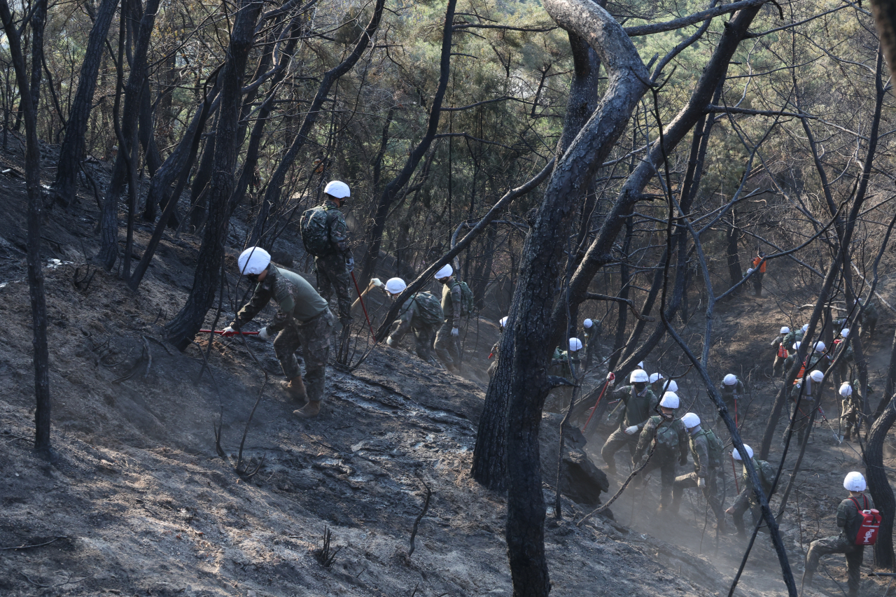 Firefighters and Army soldiers try to put out the smoldering fires on Mount Inwang in central Seoul on Monday. (Yonhap)