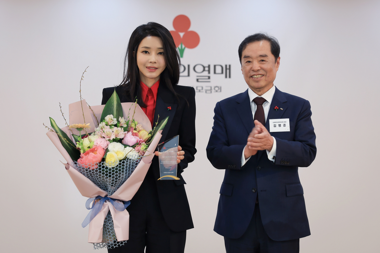 김건희 여사가 지난 4월 11일 서울 중구 사랑의열매 회관에서 김병준 사회복지공동모금회 회장으로부터 명예회장 추대패와 꽃다발을 받고 기념촬영을 하고 있다. 사회복지공동모금회는 그동안 대통령 배우자를 명예회장으로 추대해왔다. [연합]