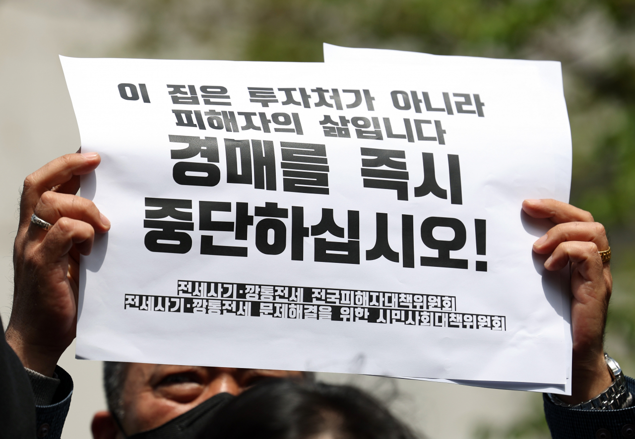 전세사기피해자전국대책위원회 한 회원이 21일 오전 인천지방법원 앞에서 열린 전세사기 피해 주택 경매 매각기일 직권 변경 요청 기자회견에서 구호 피켓을 들고 있다. [연합]