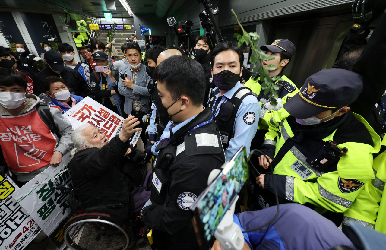 박경석 전국장애인차별철폐연대(전장연) 대표가 지난달 21일 오전 서울 지하철 5호선 광화문역에서 탑승 시위 중 지하철 탑승을 저지 당하자 국화꽃을 던지고 있다. [연합]