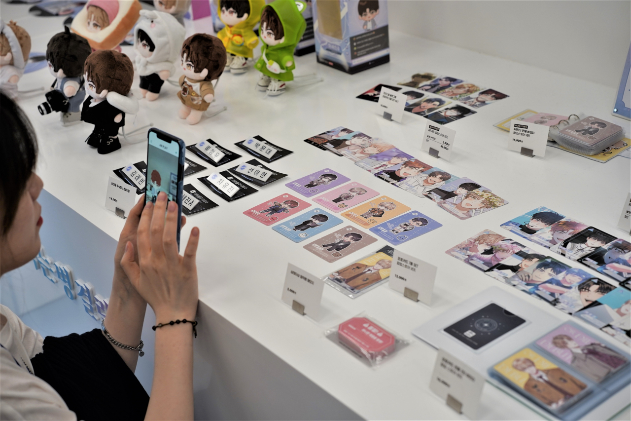 A visitor takes photos of fictional K-pop boy band TeSTAR's merchandise on Tuesday at the "Debut or Die" pop-up store at The Hyundai Seoul in Yeongdeungpo-gu, western Seoul. (Lee Si-jin/The Korea Herald)