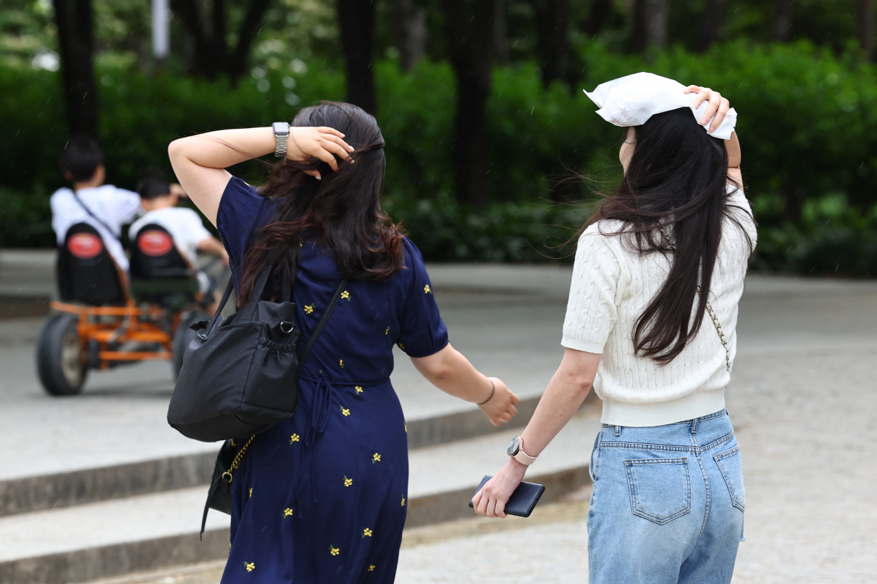 소나기가 내린 지난 6일 오후 서울 성동구 서울숲에서 휴식하던 시민들이 갑자기 내린 비에 손과 비닐 등으로 비를 막고 있다. [연합]