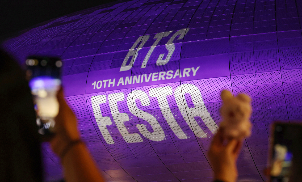 People take pictures of Dongdaemun Design Plaza's facade showing a promotional ad for BTS's 10th Anniversary Festa. (Yonhap)