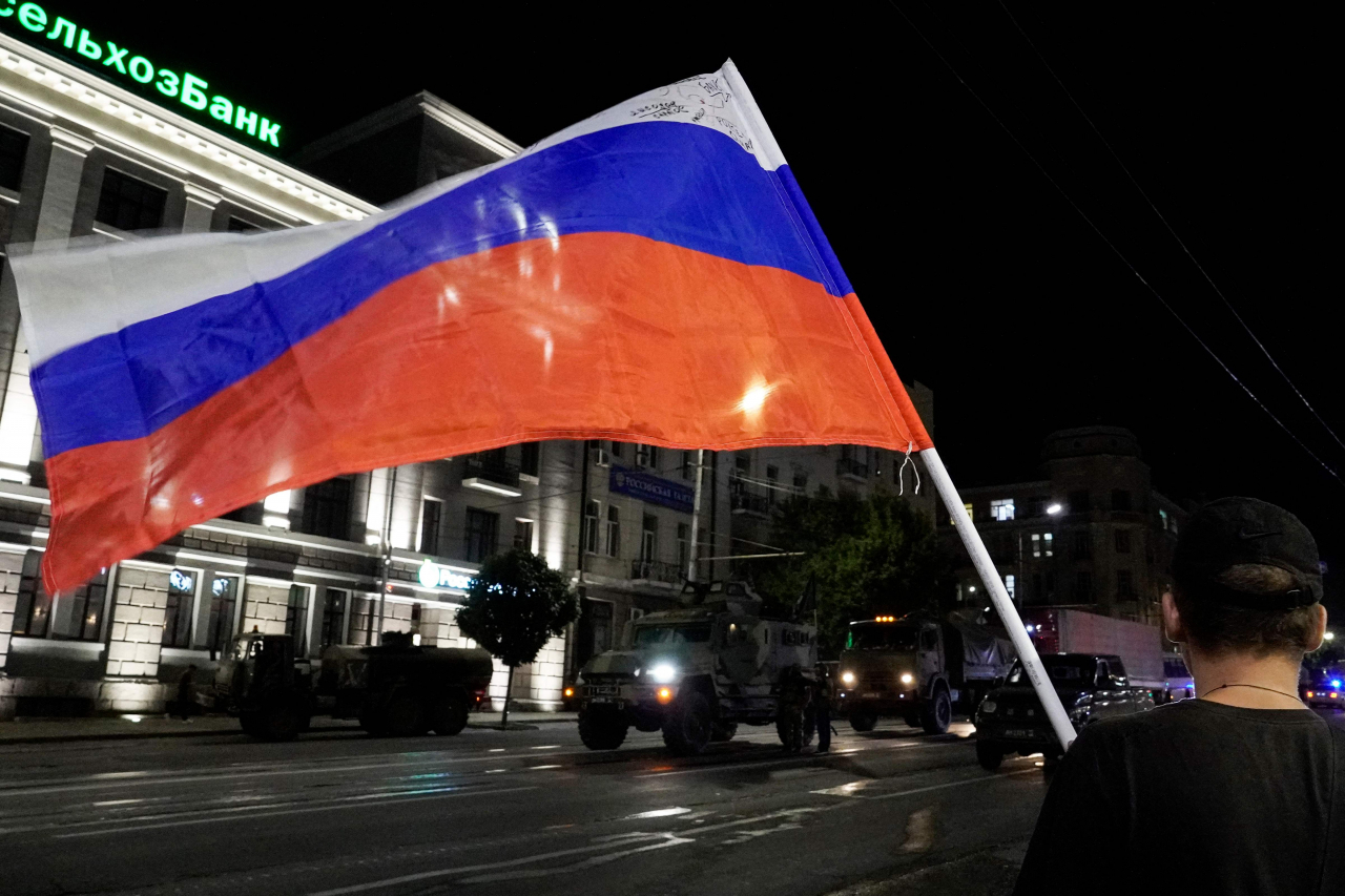 A man waves the Russian national flag as the members of Wagner group prepare to pull out from the headquarters of the Southern Military District to return to their base in Rostov-on-Don late on Saturday. Rebel mercenary leader Yevgeny Prigozhin who sent his fighters to topple the military leaders in Moscow will leave for Belarus and a criminal case against him will be dropped as part of a deal to avoid "bloodshed," the Kremlin said on Saturday. (AFP-Yonhap)