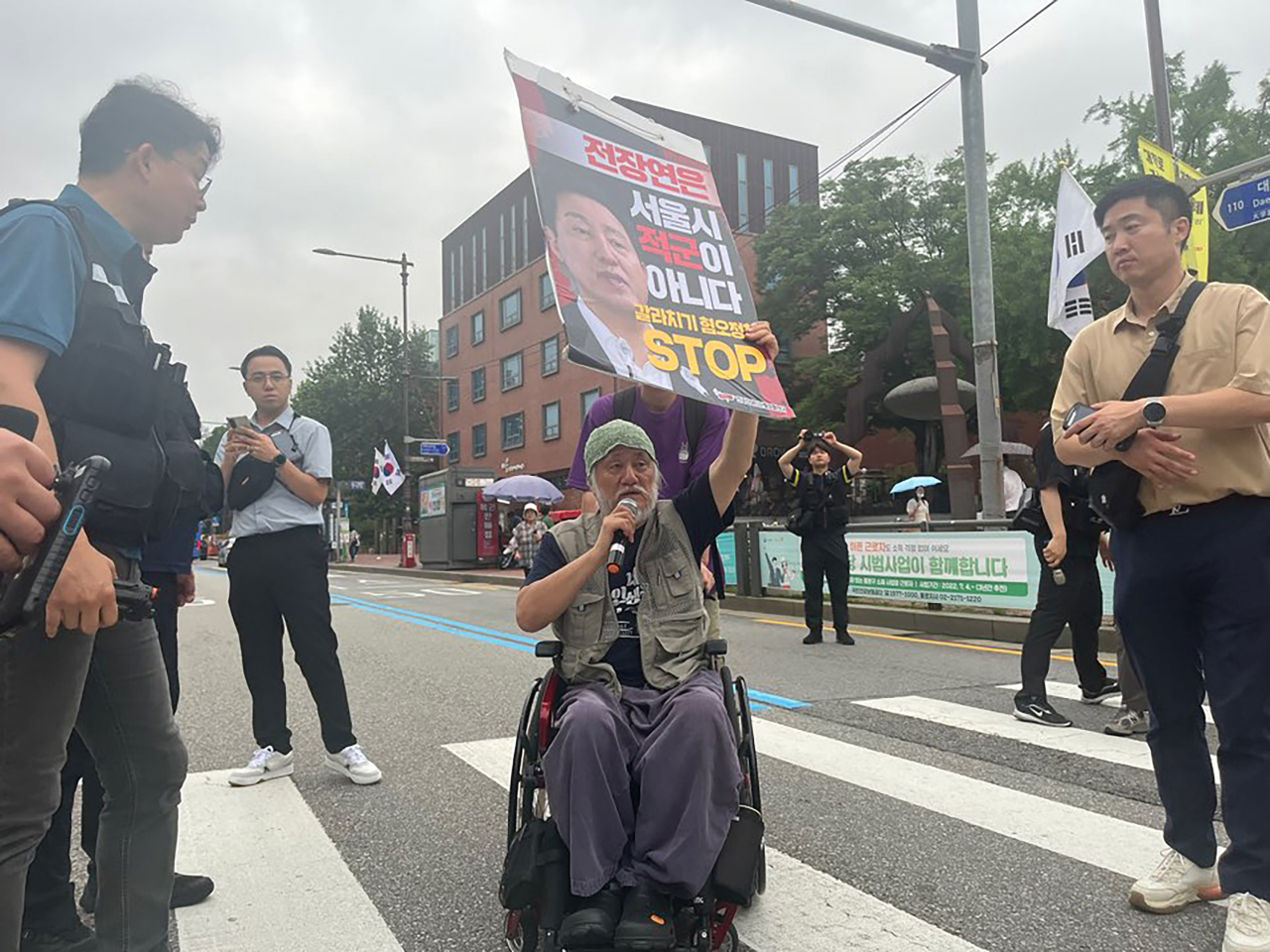 박경석 전국장애인차별철폐연대 상임공동대표가 13일 오전 서울 종로구 마로니에공원 앞 횡단보도에서 보행신호가 파란불일 때 오세훈 시장을 규탄하는 피켓을 들고 있다. [연합]
