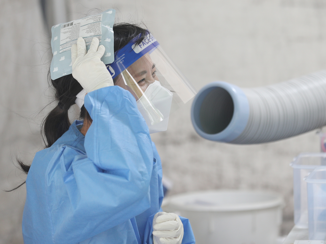 A medical staff member stands in front of an air conditioner, holding an ice pack, to beat the heat at a public health center at Daegu, July 6. (Yonhap)
