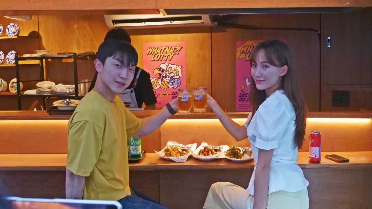 롯데월드 어드벤처 부산의 팝업스토어 광안리 ‘더 굿 바이브 로티-로티의 스낵바’에서 한쌍의 커플이 맥주를 즐기고 있다. [사진=롯데월드 부산]
