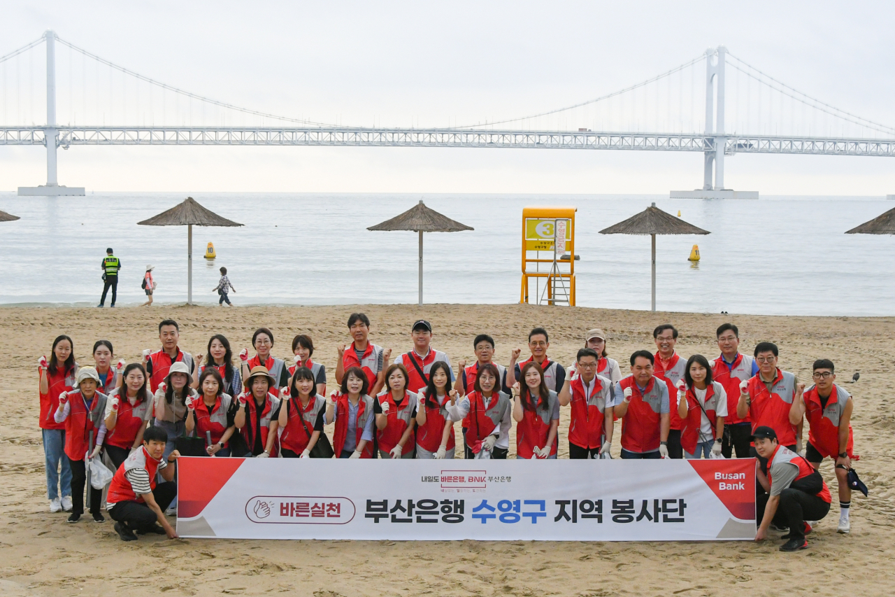 BNK부산은행 수영구 지역 봉사단이 19일 오전 부산 광안리해수욕장에서 쓰레기를 수거하는 환경정화 봉사활동에 참여한 뒤 파이팅을 외치고 있다. [사진=부산은행]