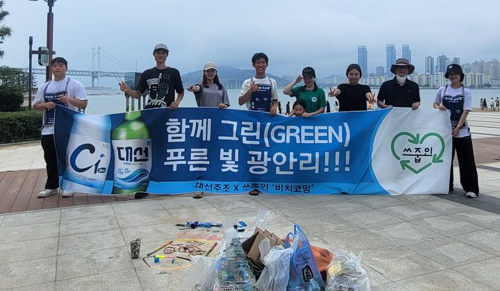 대선주조 임직원들과 ‘쓰줍인’ 회원들이 지난 19일 오전 광안리해수욕장 일대를 청소한 뒤 포즈를 취하고 있다.[사진=대선주조]