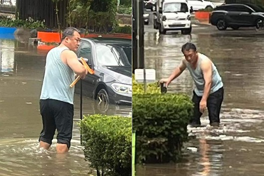 지난 23일 충북 청주시 충북대학교 앞 개신오거리 도로에서 한 시민이 기습폭우로 잠긴 도로의 배수구를 뚫고 있다. 이 시민은 국민의힘 소속 박재주 도의원으로 밝혀졌다. [온라인 커뮤니티 캡처]
