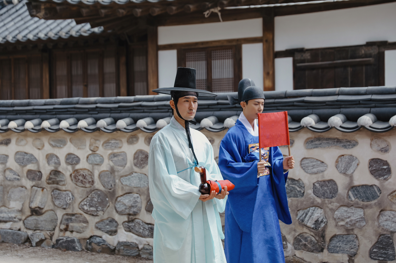 The groom (right) heads to his bride's house accompanied by gireokabeom, carrying a wooden goose. (NHV)