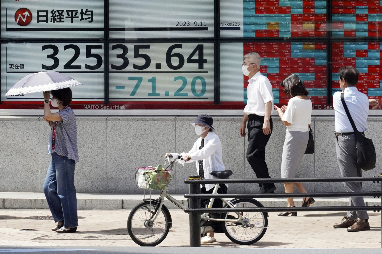 일본 도쿄의 주식시황 전광판을 지나다니는 시민들 모습 [AP]