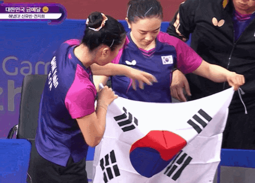 대한민국 탁구 대표팀 신유빈이 지난 2일 중국 항저우의 궁수 캐널 스포츠파크 체육관에서 펼쳐진 2022 항저우 아시안게임 탁구 여자복식 결승전에서 금메달을 딴 뒤, 기념사진을 찍기 전 태극기 방향을 바로잡고 있다. [온라인 커뮤니티 갈무리]