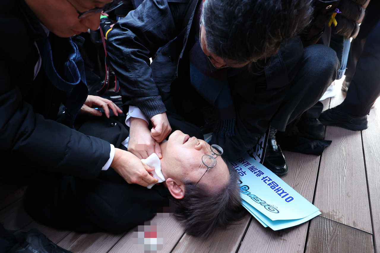 이재명 더불어민주당 대표가 2일 부산 가덕도 신공항 부지를 둘러본 후 기자들과 문답을 진행하던 중 왼쪽 목 부위에 습격을 당해 피를 흘린 채 쓰러져 있다. [연합]