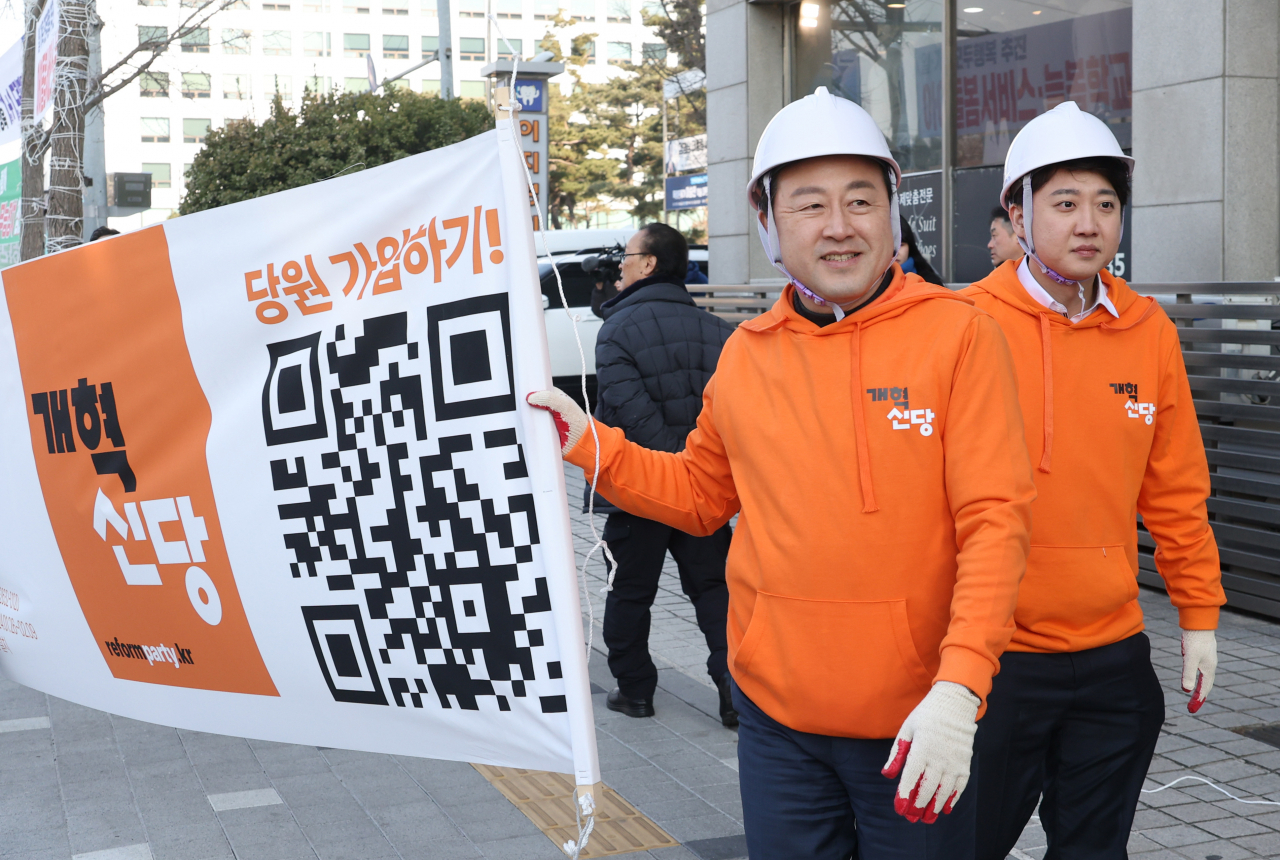 이준석 개혁신당 대표(오른쪽)와 김용남 정책위의장이 26일 국회의사당 앞 가로수에 정당 정책 홍보 현수막을 달기 위해 걸어가고 있다. [연합]