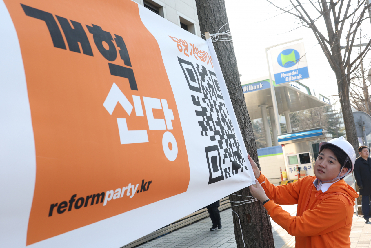 이준석 개혁신당 대표가 26일 국회의사당 앞 가로수에 정당 정책 홍보 현수막을 걸고 있다. [연합]