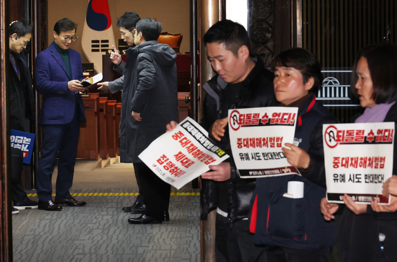 더불어민주당 박주민 원내수석부대표가 1일 국회에서 열리는 의원총회에서 동료들과 대화를 나누는 가운데 정의당과 노동계 관계자들이 회의장으로 향하는 의원들을 향해 중대재해처벌법 유예 반대 피케팅을 하고 있다. [연합]