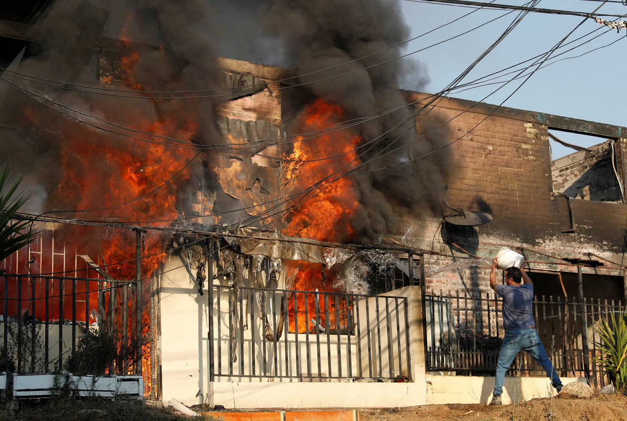 A man tries to extinguish a fire burning a house during the spread of wildfires in Vina del Mar, Chile on Feb. 3. (Reuters-Yonhap)
