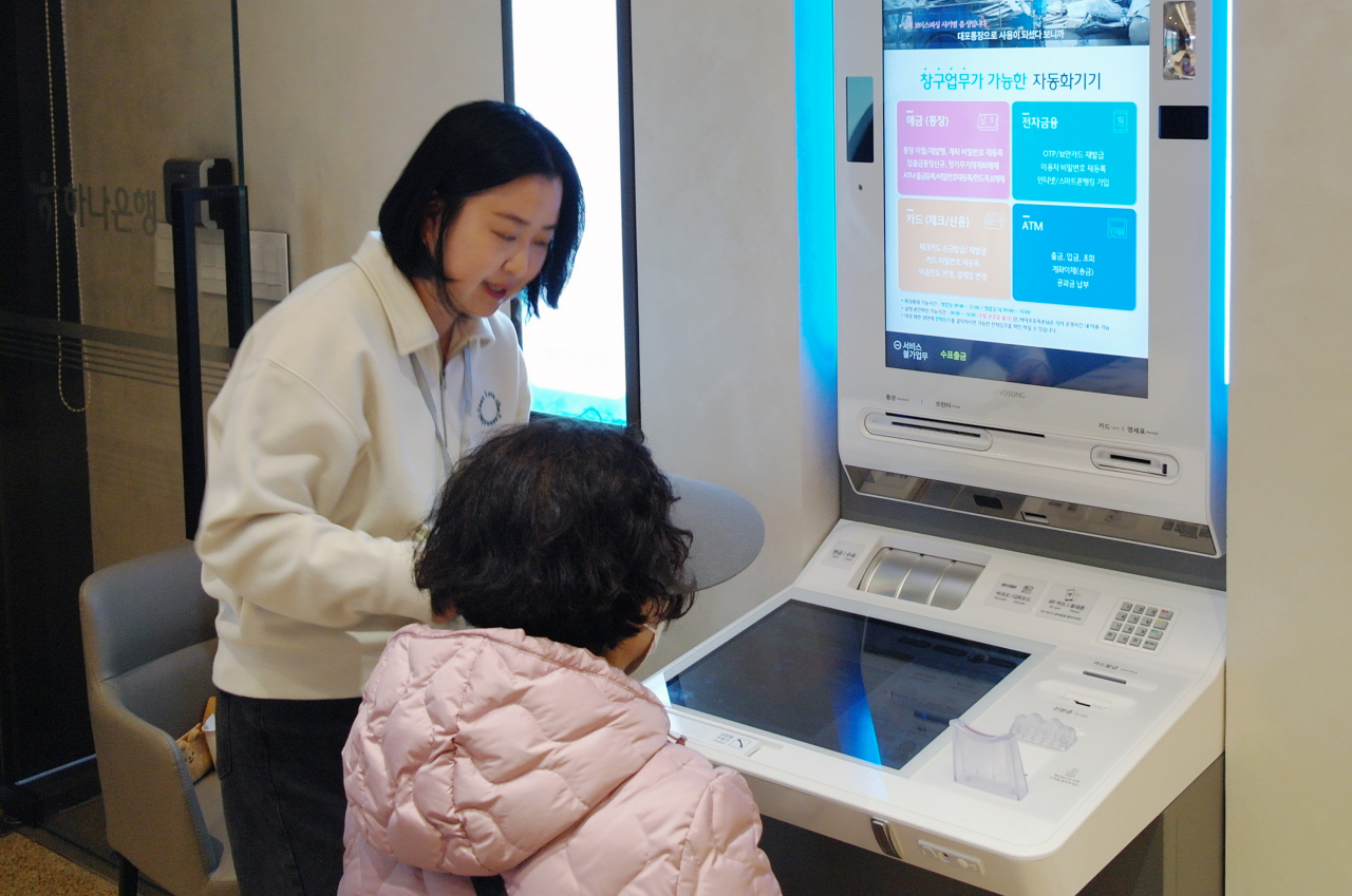 A Hana Bank employee (left) helps an old lady in using the ATM machine at the bank‘s branch in Tanhyeon-dong of Goyang in Gyeonggi Province. (Hana Bank)