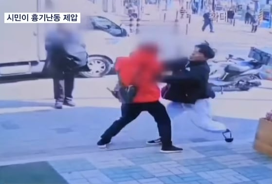대낮에 서울의 한 거리에서 50대 남성이 흉기를 들고 거리를 돌아다니자 이를 발견한 시민이 인파가 적은 곳으로 유인해 흉기 난동을 저지했다. [MBN 보도화면 갈무리]