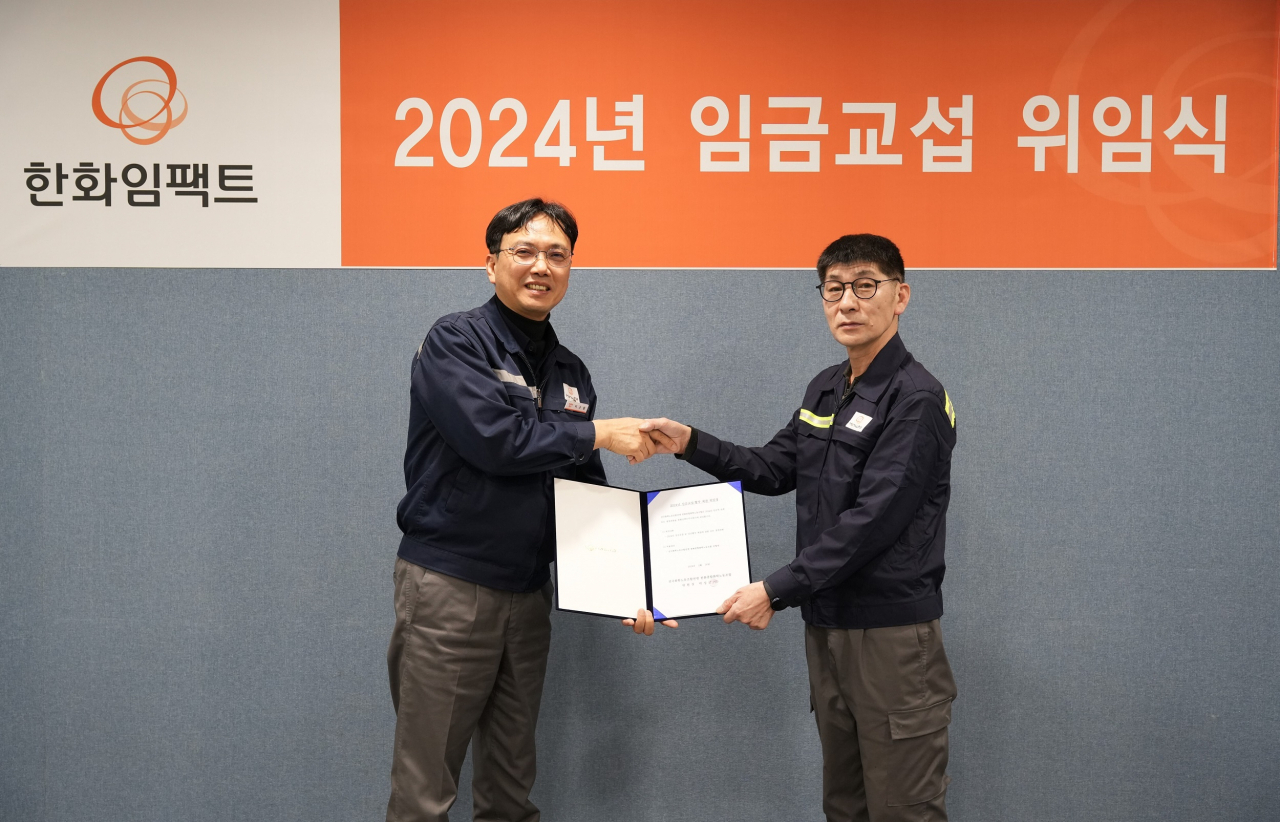 이근철(왼쪽) 한화임팩트 총괄공장장과 박성군 노동조합위원장이 지난 12일 한화임팩트 울산사업장에서 열린 2024년 임금교섭 위임식에서 기념촬영을 하고 있다. [한화임팩트 제공]