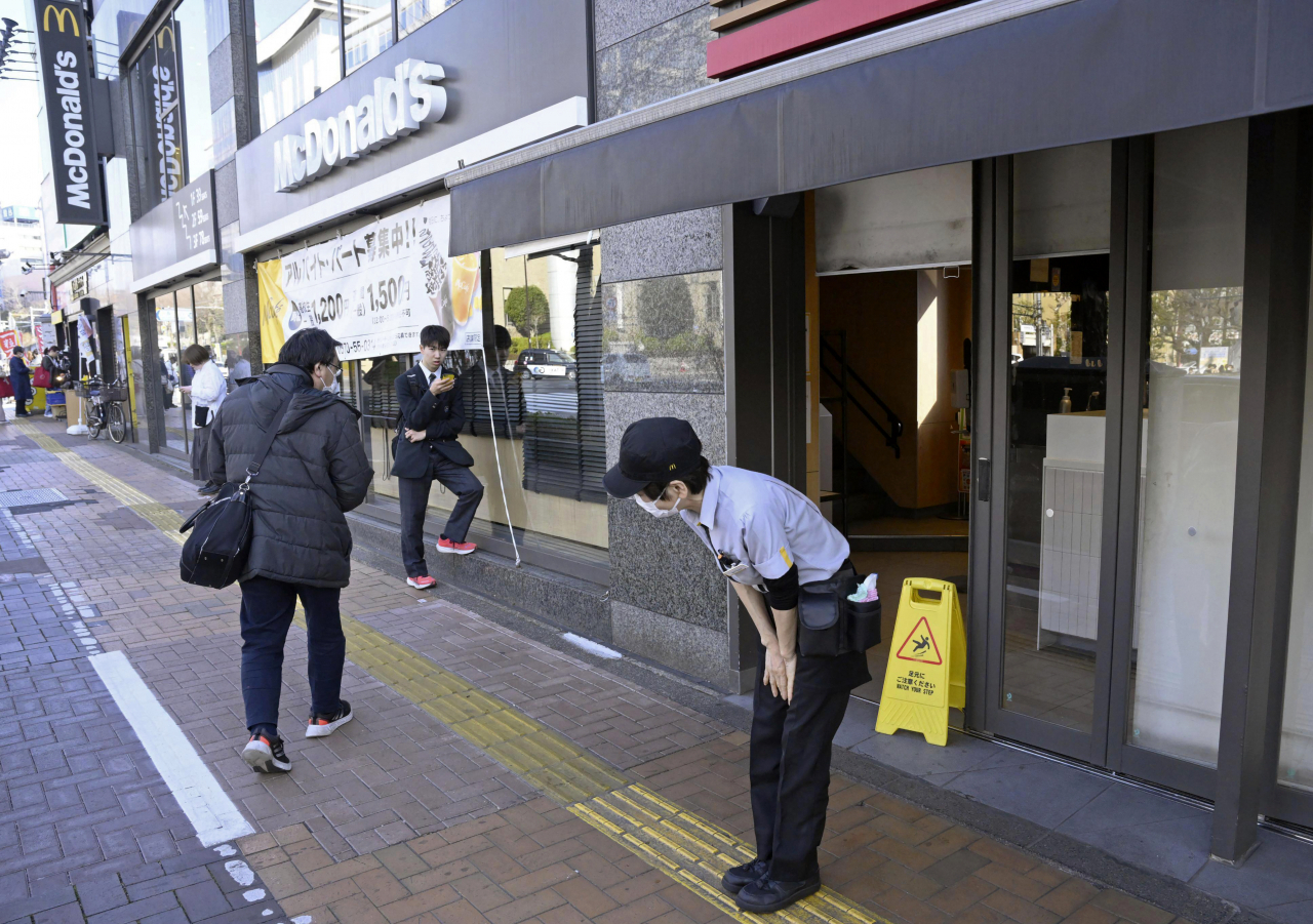 15일 일본 도쿄에서 매장의 전산 장애로 주문을 처리하지 못해 맥도날드 직원이 매장 앞에서 고개를 숙이고 있다. [AP]