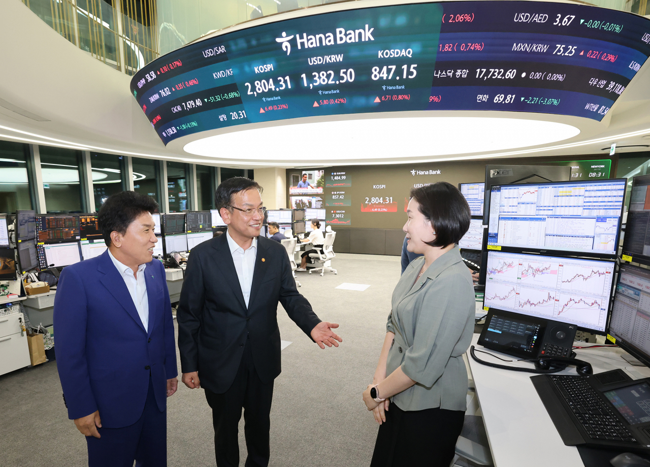 7월 1일 외환시장 개장시간 연장 첫날을 맞아 오후 9시 30분경, 최상목(사진 왼쪽 두 번째) 부총리와 함영주(왼쪽 첫 번째) 하나금융그룹 회장이 하나은행 딜링룸 직원과 변경된 제도 시행에 대한 의견을 나누고 있다.[하나금융그룹 제공]