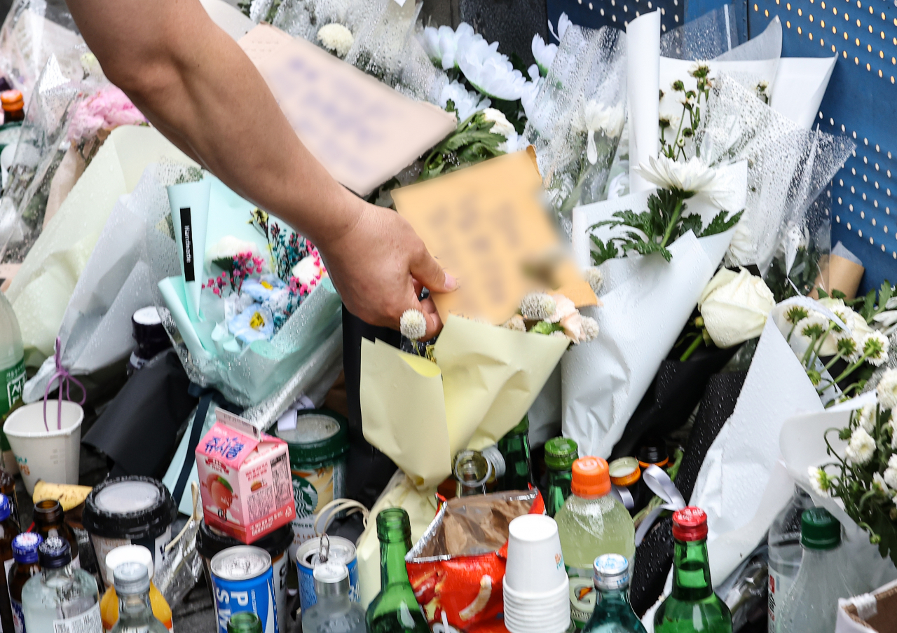 경찰관들이 5일 오전 서울 중구 시청역 인근 역주행 사고 현장에 마련된 추모 공간에서 추모글을 빙자한 조롱 표현 쪽지들을 수거하고 있다. [연합]