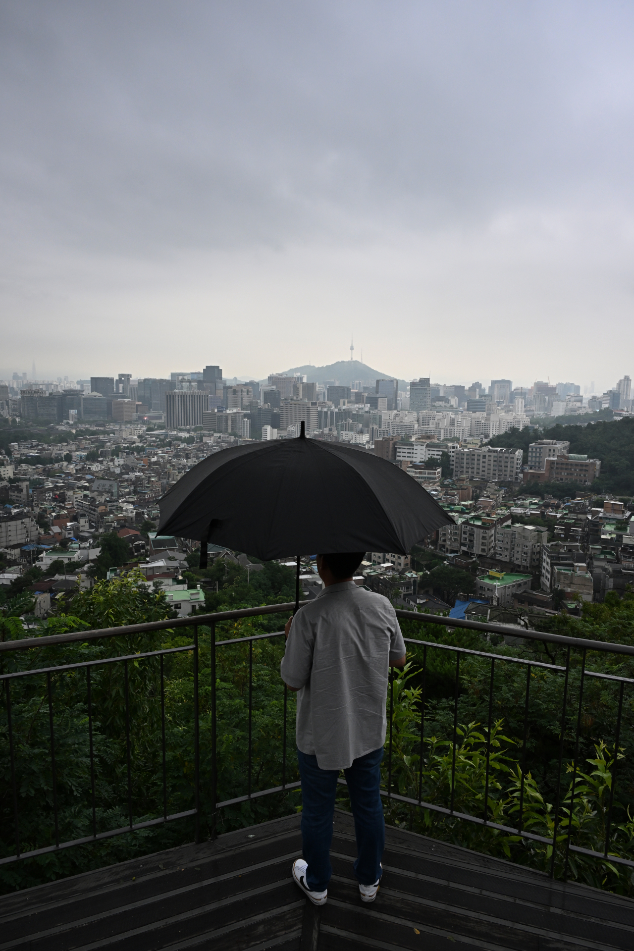 10일 서울 종로구 인왕산 전망대에서 한 시민이 우산을 쓰고 서울 도심 일대를 바라보고 있다. 임세준 기자