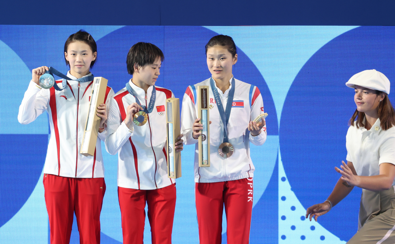 6일(현지시간) 프랑스 파리 아쿠아틱센터에서 열린 2024 파리올림픽 다이빙 여자 10ｍ 플랫폼 결승에서 동메달을 딴 북한 김미래(오른쪽)가 시상식에서 셀카 세리머니를 위해 진행자로부터 갤럭시 스마트폰을 건네받자 난감해 하고 있다. [연합]