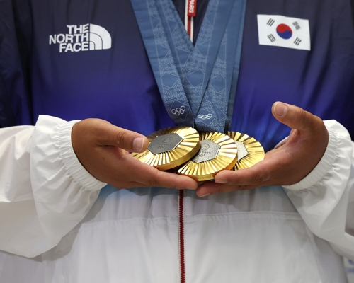 2024 파리 올림픽에서 양궁 남자 단체전, 혼성 단체전, 개인전에서 금메달을 차지한 김우진이 6일 오전 인천국제공항을 통해 귀국한 뒤 금메달을 들어보이고 있다. [연합]