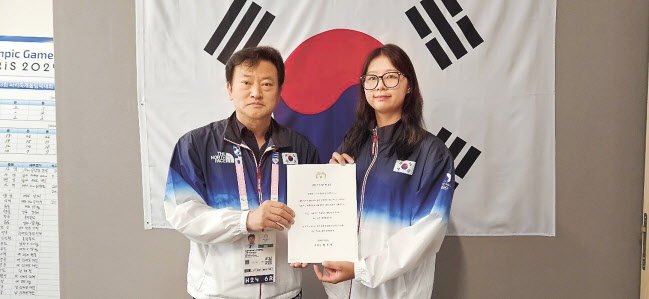 정강선(왼쪽) 한국 선수단장이 5일(현지시간) 양궁, 수영, 사이클 종목 선수들의 퇴촌식에서 양궁 3관왕 임시현에게 윤석열 대통령의 축전을 전달하고 있다. [정강선 단장 제공]