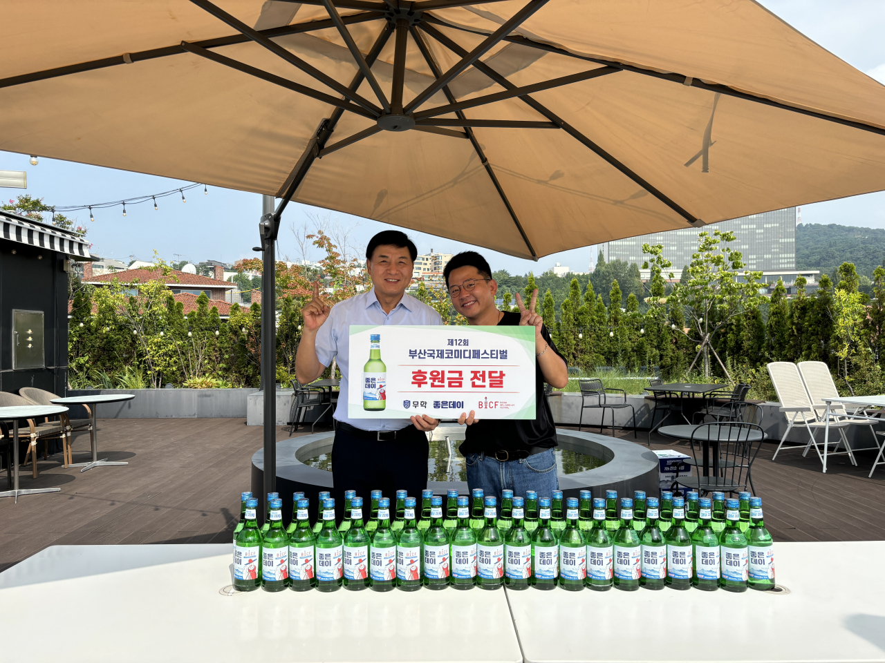 지난 10일 서울시 용산구 무학 굿데이빌딩에서 최재호 무학 회장(사진 왼쪽)이 김준호 부산국제코미디페스티벌 집행위원장에게 후원금을 전달하고 기념 촬영하고 있다. [사진=무학]