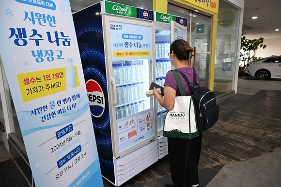 부산 기장군 기장시장 공영주차장에 설치된 무료 생수 나눔 냉장고에서 주민이 생수를 꺼내고 있다. [사진=기장군]