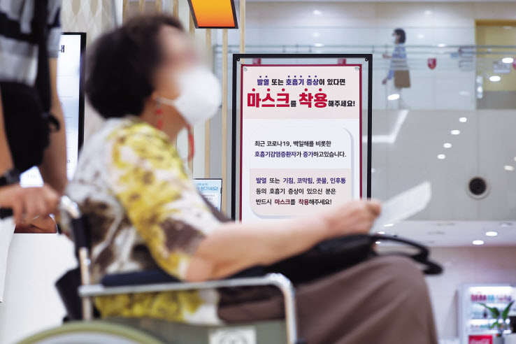 지난 22일 서울 구로구 고려대 구로병원에 코로나19 감염 환자 증가 등으로 인한 마스크 착용 권고 안내 배너가 설치돼 있다. 배너 앞을 휠체어를 탄 환자가 지나가고 있다. [연합]