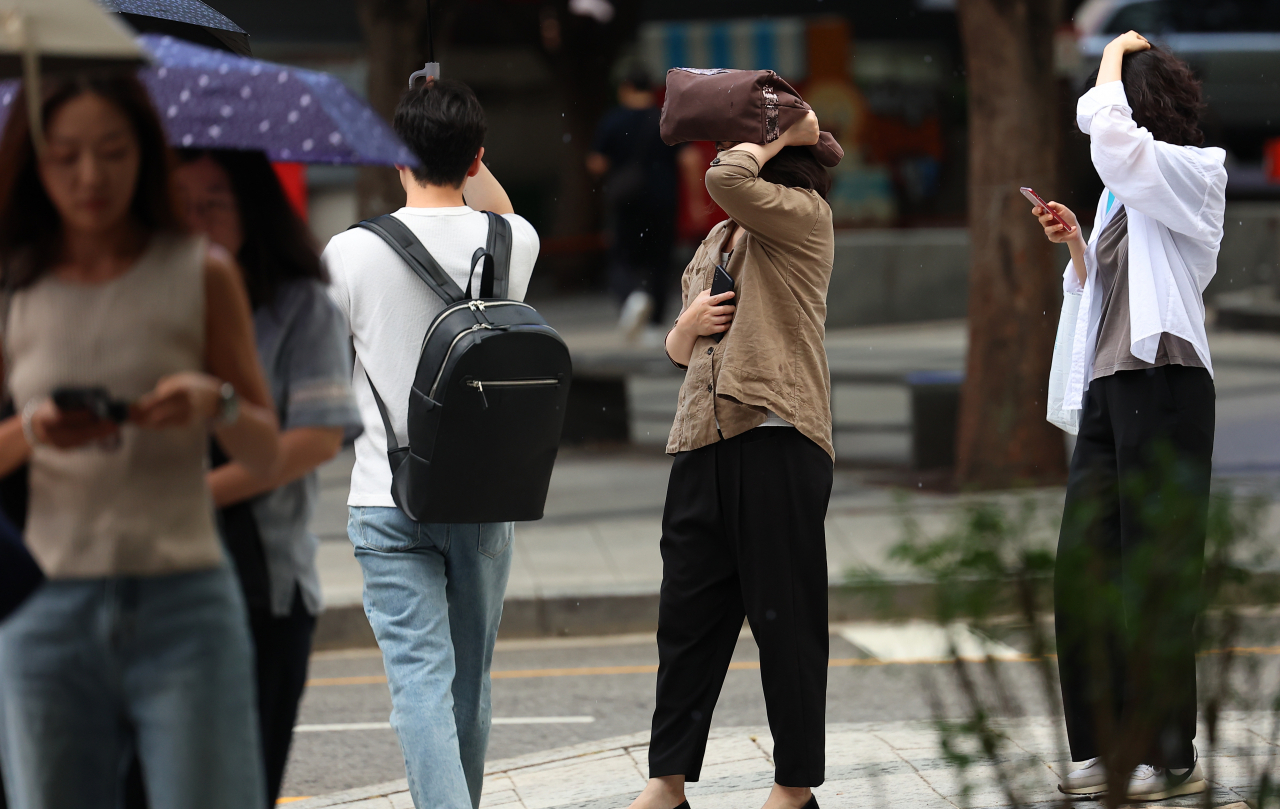 서울지역에 퇴근길 소나기가 내린 19일 오후 서울 세종로사거리 인근 버스정류장에서 우산을 준비하지 못한 시민들이 손과 가방으로 머리를 가린 채 버스를 기다리고 있다. [연합]
