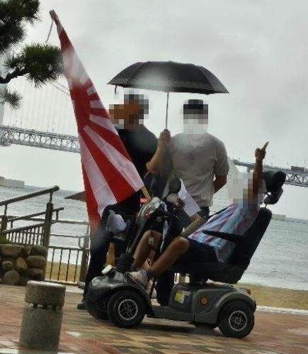 28일 오전 부산 수영구 광안리해수욕장에서 70대 남성이 자신의 전동 휠체어에 욱일기를 내걸고 돌아다니고 있다. [온라인 커뮤니티 갈무리]