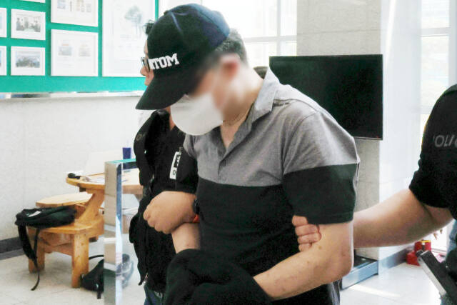 직장 동료 살해 혐의를 받고 있는 50대 남성이 수갑을 찬 채 경찰서 내부로 들어오고 있다. [사진 연합뉴스]