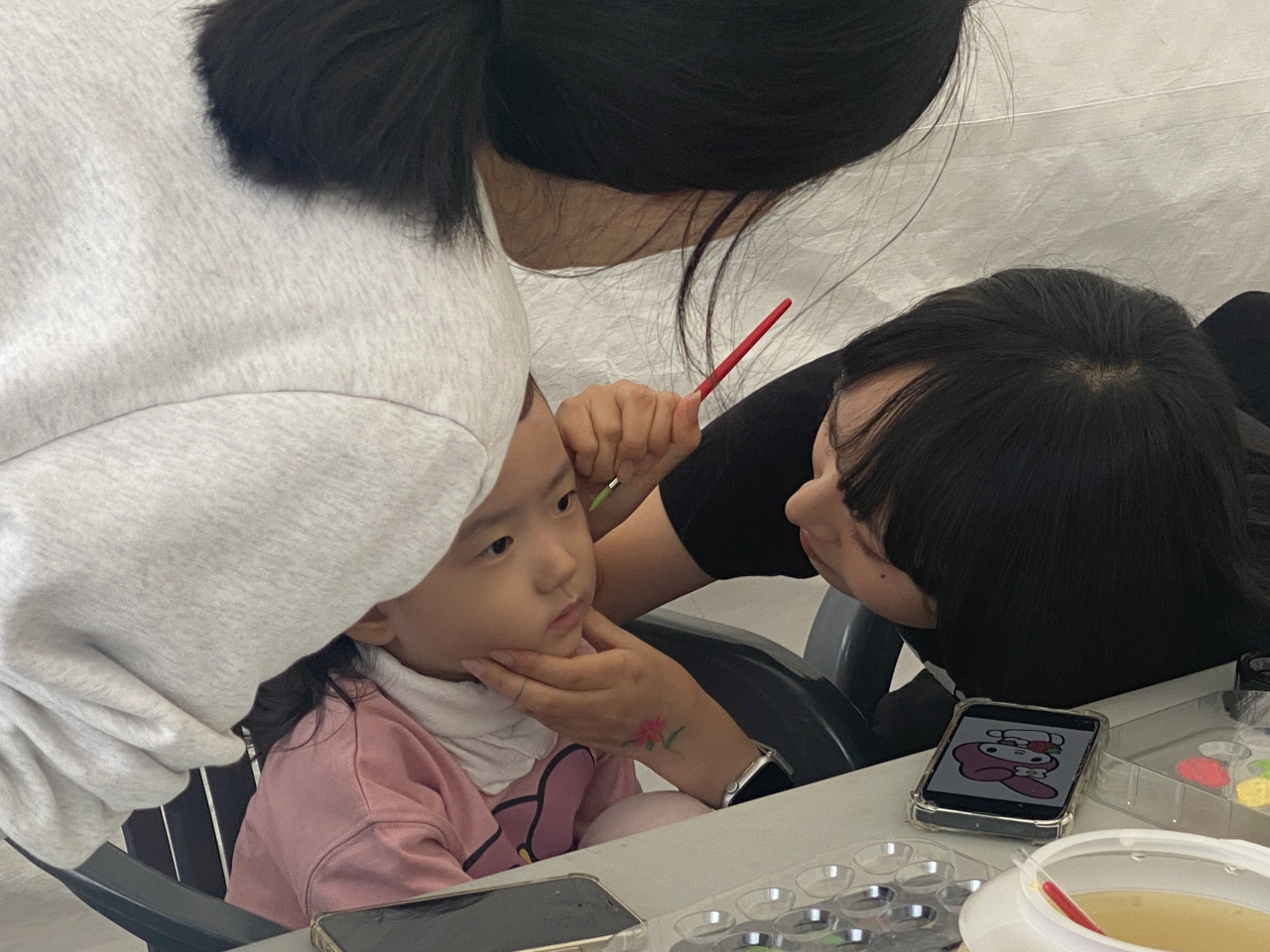 An art student from Kaywon University offers face painting to a young visitor at the Wellness Seoul 2024 booth, Sunday. (Hwang Joo-young/The Korea Herald)