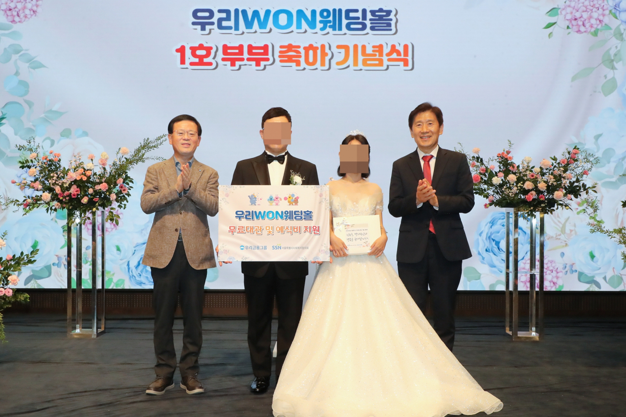 우리은행은 취약계층 신혼부부의 결혼식을 위해 우리금융 본사 사옥 웨딩홀을 무료로 대관해 주는 ‘우리 WON 웨딩홀’ 1호 부부가 탄생했다고 14일 밝혔다. 13일 진행된 결혼식에서 조병규(맨 왼쪽) 우리은행장과 ‘우리 WON 웨딩홀’ 1호 부부, 김현훈 서울특별시사회복지협의회장이 기념촬영을 하고 있다. [우리은행 제공]