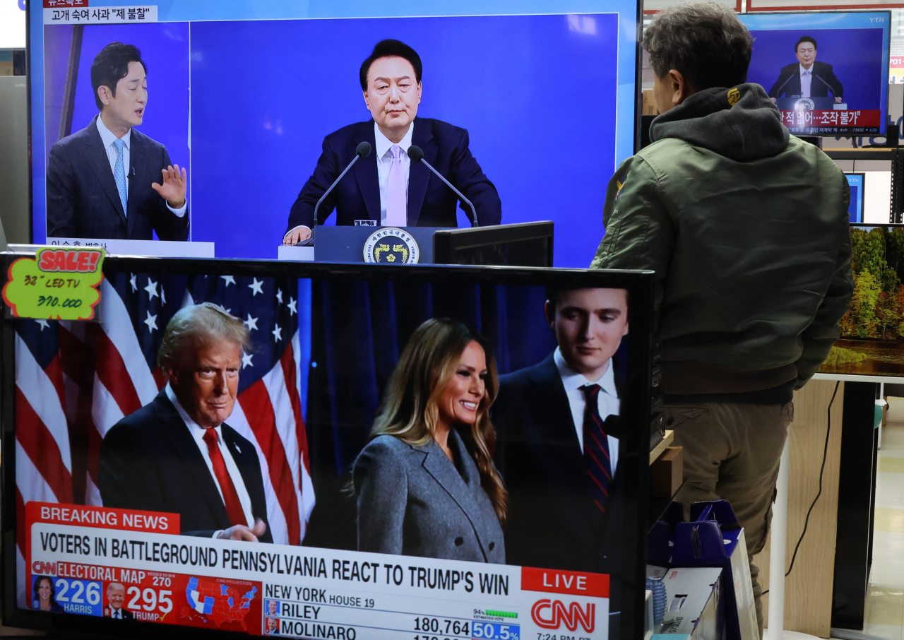 A man watches President Yoon Suk Yeol's televised address and press conference marking the second half of his term while a television screen in the front displaying results of the US presidential election at an electronics market in Yongsan, Seoul, Thursday. (Yonhap)