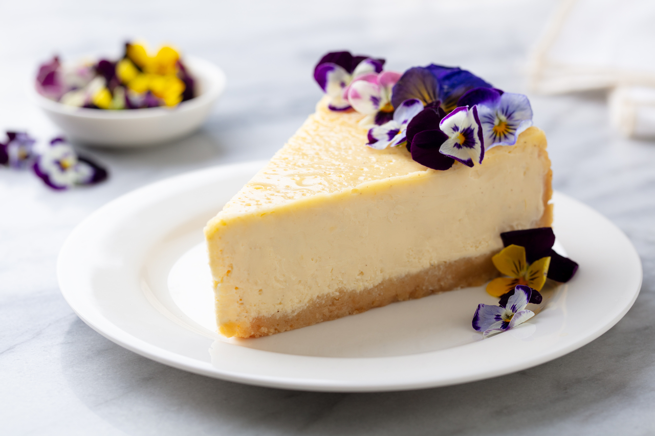 Cheesecake decorated with edible flowers on white plate. Marble background.