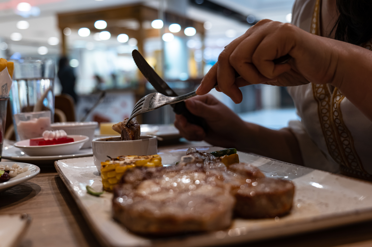 Close-up partial view of woman enjoy eating steak with fork and knife in restaurant