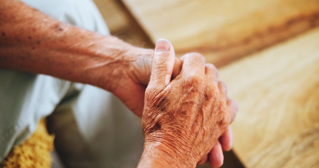 Senior, hands and wrinkles on sofa alone with thinking, sad or muscle health for arthritis at home. Elderly person with palms together Parkinson or massage of fingers for pain on couch from above