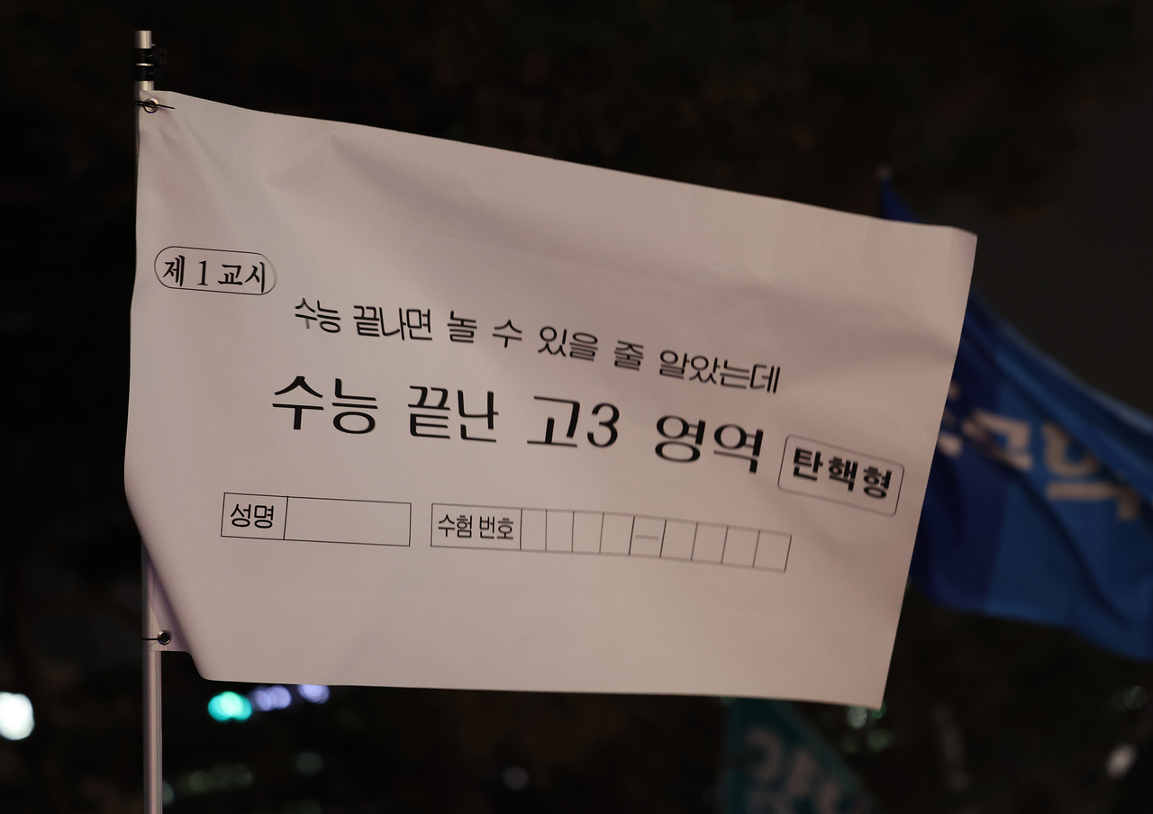 지난 12일 오후 서울 영등포구 국회 앞에서 열린 윤석열 대통령 탄핵 촉구 촛불 집회에 참석한 한 시민이 ‘수능 끝나면 놀 수 있을 줄 알았는데’라고 적힌 깃발을 들고 있다. [연합뉴스]