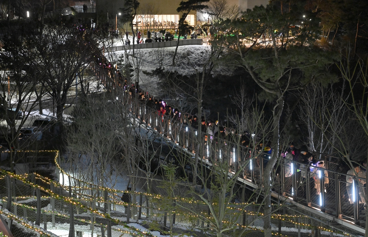 Visitors stroll along a trail lined with illuminated trees leading to the observatory deck of Aegibong Peace Ecopark in Gimpo, Gyeonggi Province, Saturday. Every year, the park, a symbol of the divided Korean peninsula, transforms its Christmas celebration into a beacon of hope and peace, illuminating the spirit of unity through the presence of its visitors. (Lee Sang-sub/The Korea Herald).